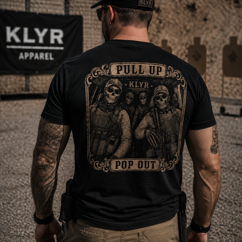 Rear lifestyle view of the black KLYR Pull Up Pop Out Tee showcasing the large vintage tactical team back graphic at an outdoor shooting range.