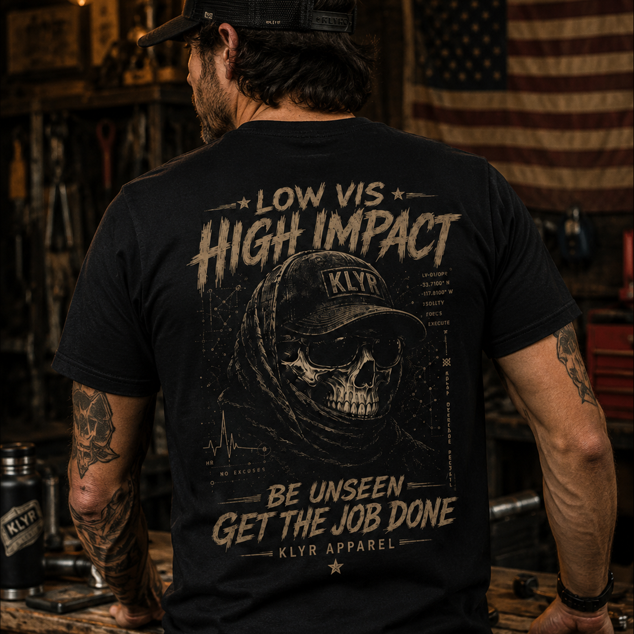 Rear lifestyle view of the black KLYR Low Vis Tee showcasing the tactical skull back graphic in a workshop setting.