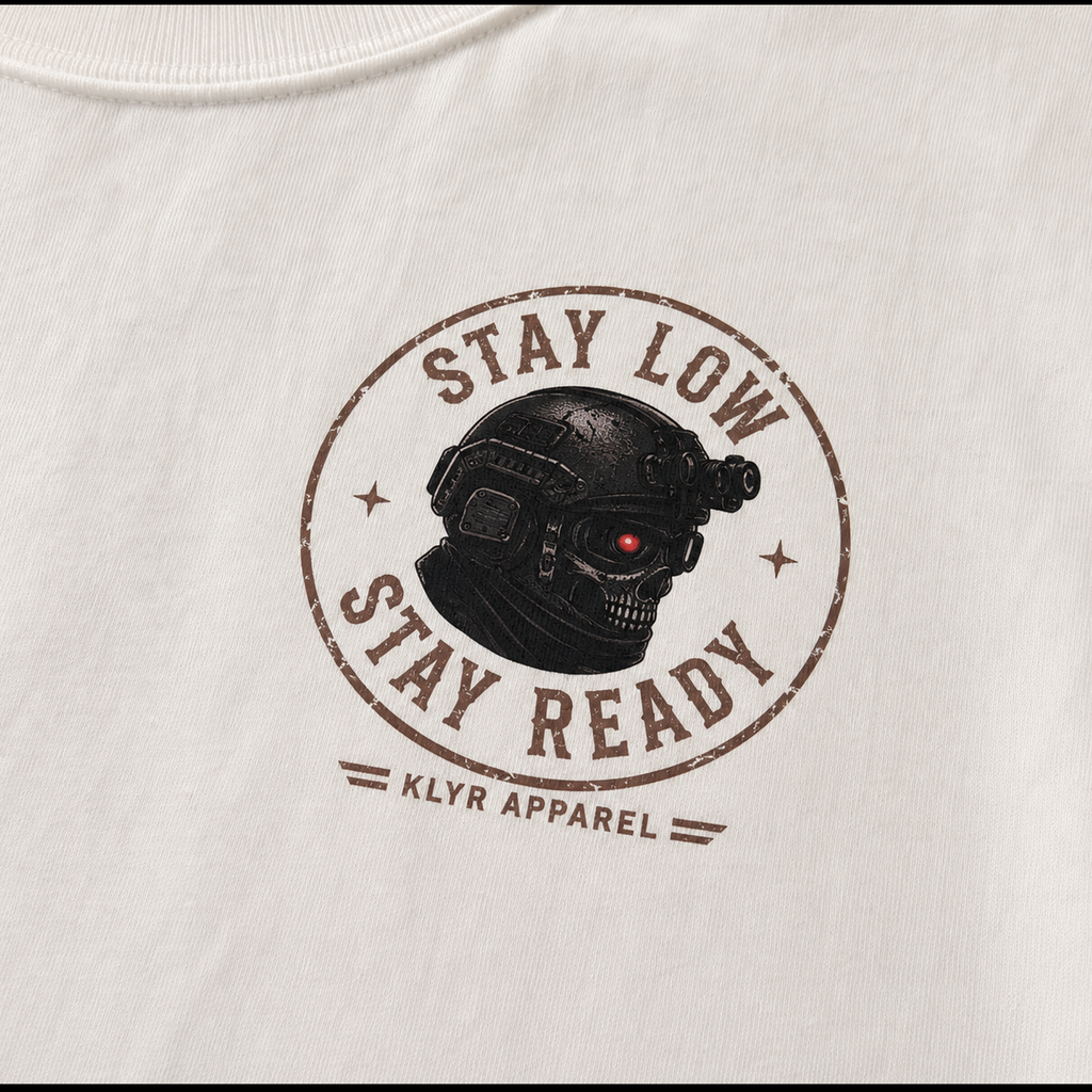 Detailed close-up of the Stay Low Stay Ready tactical helmet chest logo printed on the white KLYR Stay Low Stay Ready Tee.